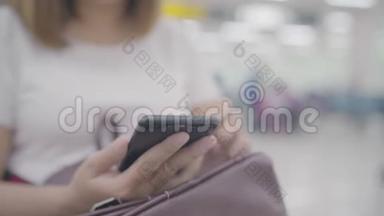 快乐的亚洲女人在机场登机口等待航班时，在候机大厅使用和检查她的智能手机。